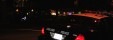 In the darkness of night, a black car with the word "police" in white on the trunk can be seen in the foreground.