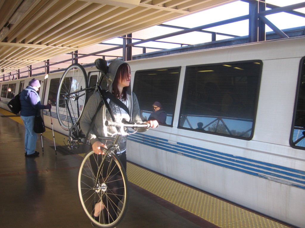A cyclists in a hoodie holds onto a bike on a BART platform as the train arrives
