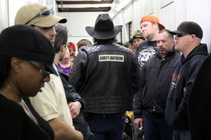 ForrestBackOfJacket Auctioneer Forrest O’Brien (center) is a character. O’Brien arrived at PayLess Self Storage in a black leather Harley-Davidson jacket, black Ray-Ban Sunglasses, and a dark brown cowboy hat, with toothpicks stuck in the brim. O’Brien’s tan leather wallet sticks out of his back pocket, attacked to his crisp dark jeans with a gold chain. His handlebar mustache is neatly groomed and his long hair just barely peeks out from beneath his hat. Worn-in brown leather cowboy boots complete the look.
