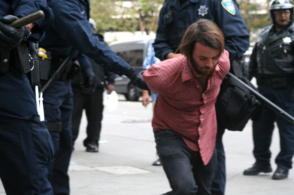 Oakland police officers restrained and handcuffed a protestor on the corner of Broadway and 14th Street, across the intersection from the plaza where the encampment had existed. Photo by Brittany Schell.