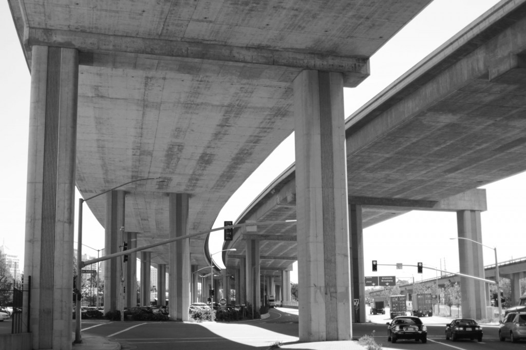 Cars under two freeway underpasses. The photo is in black and whitte