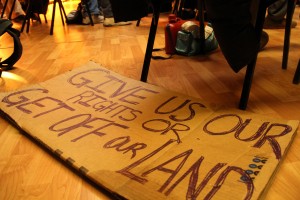 A homemade sign on brown cardboard reads: "Give us our rights or get off our land."