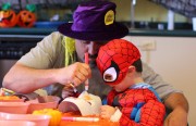 3 year old boy dressed as spiderman coloring a mask with his father.