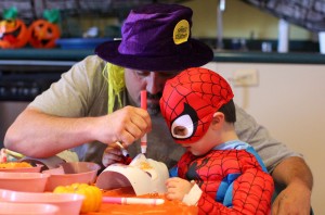3 year old boy dressed as spiderman coloring a mask with his father.