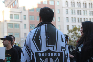 A man, draped in an Oakland Raiders flag, stands in front of City Hall