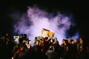 Ronald Cruz, center, an organizer with By Any Means Necessary (BAMN), directs protesters back to downtown Oakland from the 580 freeway as smoke from a burning mattress billows behind him. November 24, 2014. (Photo by Bonnie Chan)
