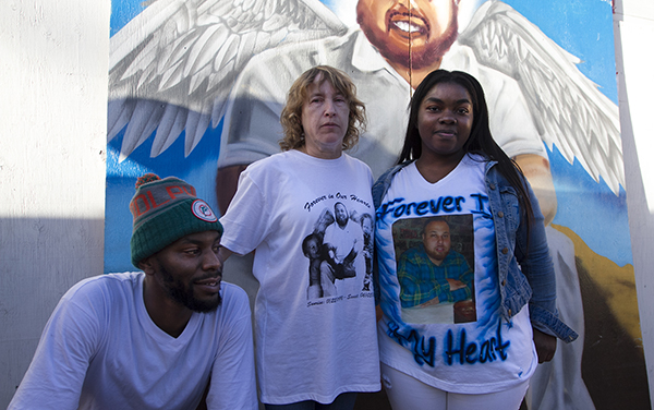 Jay Belser, Isaiah’s friend (left), Phylis, his mother (middle) and Florence Price, is close friend whom he dated in high school (right) stand in front of the mural at the memorial block party. Photo by Gina Pollack.