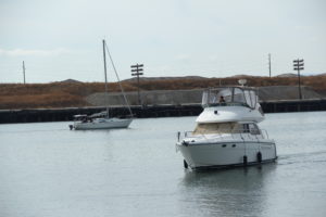 Boats go by in the harbor in front of Jack London Square, drawing many onlookers.