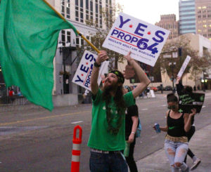 Supporters of Prop 64, Chris Conway, left, Danielle Negrin, right, gathered outside the Patient ID Center on Broadway in Downtown Oakland urging all in the street to legalize cannabis. Photo by Nate Shiedlower.