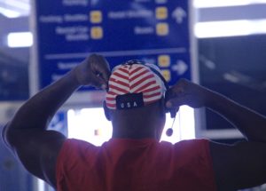 A man with a USA cap and a headset waits by the baggage claim in the Oakland International Airport.