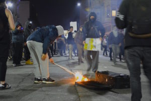 Protestors fan a fire, burning signs and a luggage on Washington St. in Oakland. Photo by Sawsan Morrar.