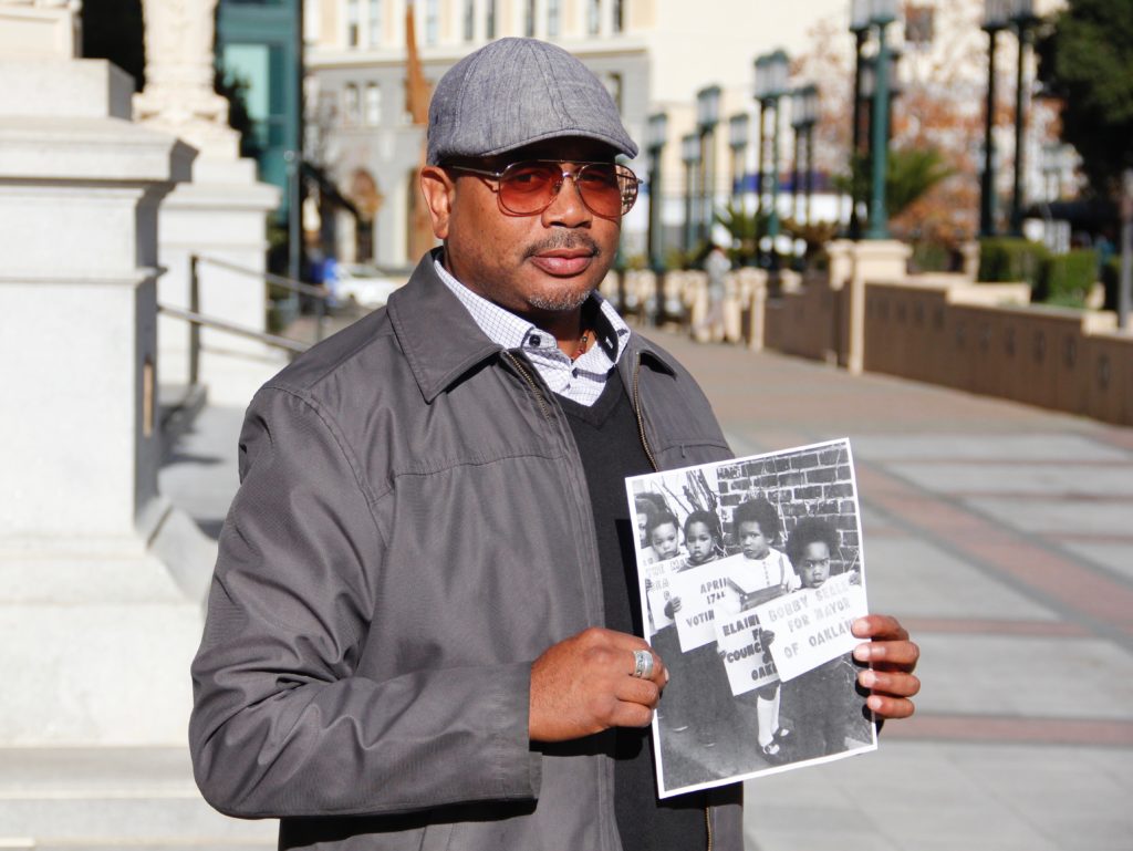 Gregory Lewis holds up a childhood photograph of himself campaigning for Bobby Seale. Lewis, who now works as a lawyer in downtown Oakland, attributes the Oakland Community School with much of his success.