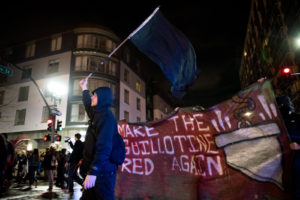 A protester with a black flag is followed by a banner which reads "Make the Guillotine Red Again", in reference to President Donald Trump's popular campaign slogan. Photo by Rosa Furneaux.