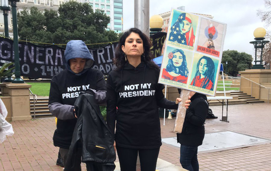 Demonstrator Yael Martinez holds a picket sign in front of Oakland City Hall, where a march is planned for noon. ”Its alarming this is where we are in 2017,” she said. Photo by Abner Hauge.