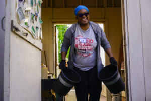 Volunteer, Tonya Love, smiles as she carries two buckets of compost at the Memorial Tabernacle Church for a lawn party to restore the church's garden on Saturday, May 6, 2017. (Yesica Prado/Oakland North)