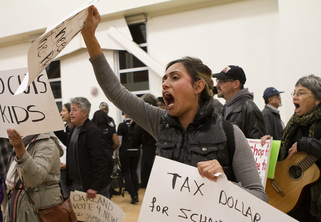 Child development teacher Natalia Hernandez carries signs and chants 'no cuts to kids,' during a protest against budget cuts at the OUSD school board meeting on Monday evening at La Escuelita. Photo by Anne Wernikoff