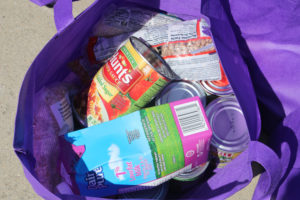 A purple bag with canned food and dry goods.