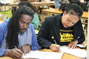 Mayoral candidate Cat Brooks (right) and her husband fill in their ballot while surrounded by cameras at Brooks’ West Oakland polling place. Photo by Katey Rusch.