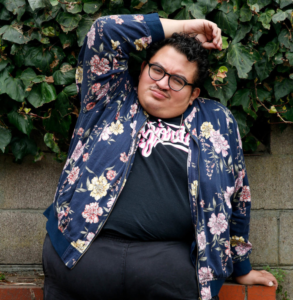 Caleb Luna, an apple-shapped fat femme, poses outside of their home in West Oakland.