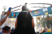 A child sits on an adult’s shoulders to see above the dense crowd during one of the traditional performances by Aztec dancers at the Unity Council’s Día de los Muertos festival on November 4. Just ahead, a sign hangs from a neighborhood arch, with artwork by local artist Eduardo Chaidez.