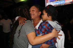 Brooks (center) hugs the coordinator of Tuesday’s campaign watch party, Jessica Moncada-Konte,(left) while holding a supporter’s son.