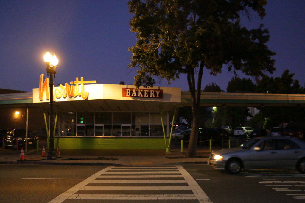 A crosswalk leads to a green, mid-century drive thru building. A sign says "Merritt Bakery," but the building is empty. This used to house the Kwik Way drive-thru.