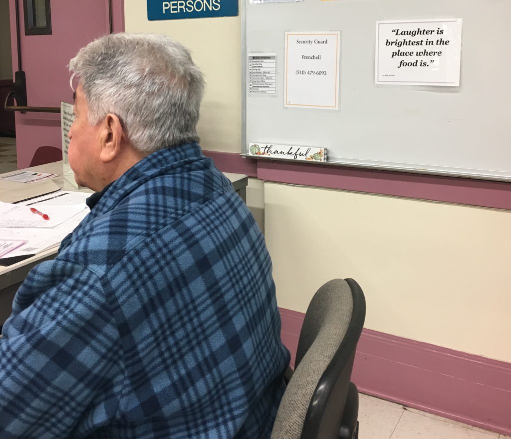 Juan, seated, checks people in for lunch at the Downtown Oakland Senior Center.