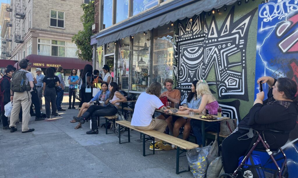 People sit and stand outside Tamarack bar in downtown Oakland, enjoying food and drink at a fundraiser for Street Spirit.