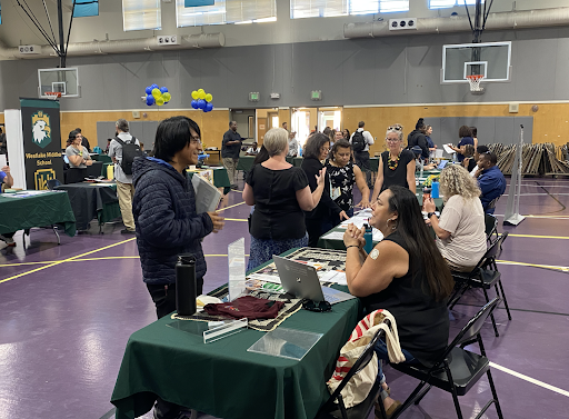 OUSD recruiters sit behind tables as a few potential job applicants ask them questions.