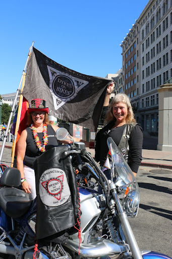 Two women stand on each side of a motorcycle, wearing black.