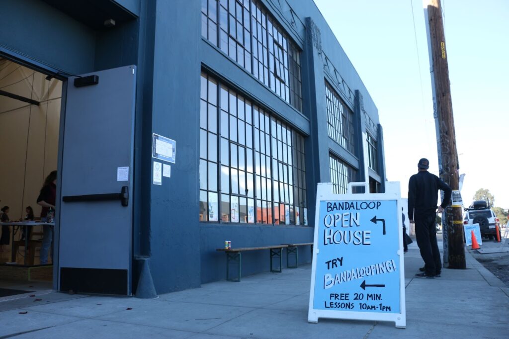 Outside a blue building with lots of windows is a blue sign with the words: Bandaloop Open House. Try Bandalooping! Free 20 min lessons 10 am-1pm