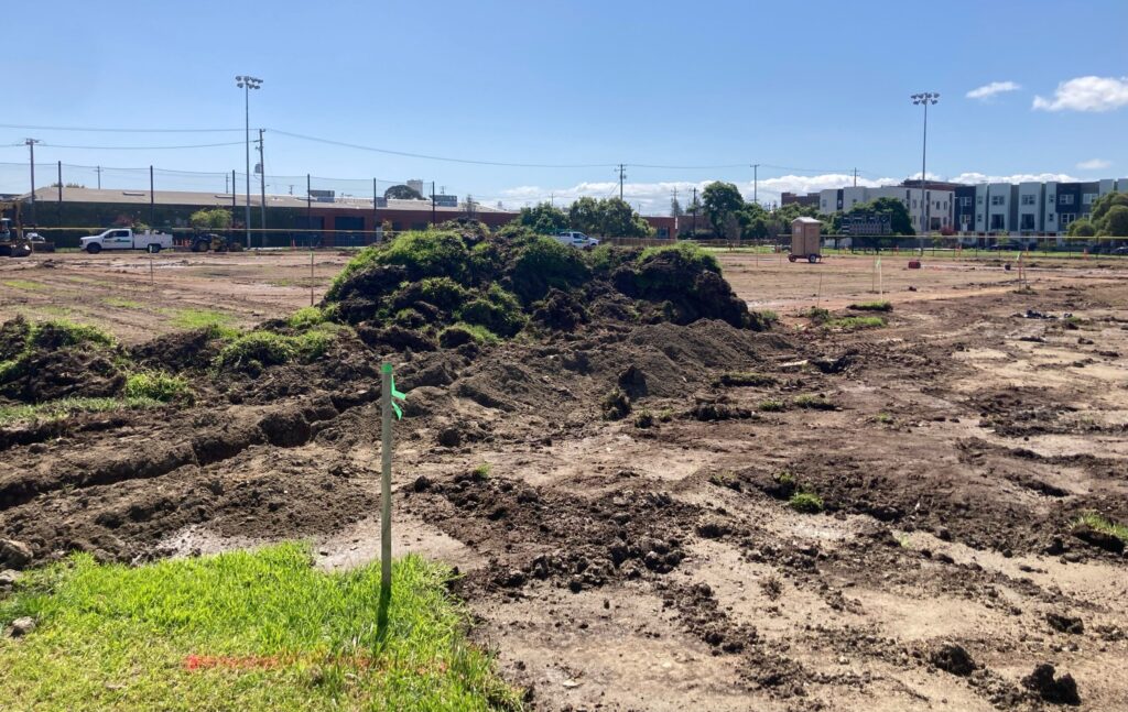 A ripped up baseball field is a mount of grassy dirt, with a squat building beyond the outfield.