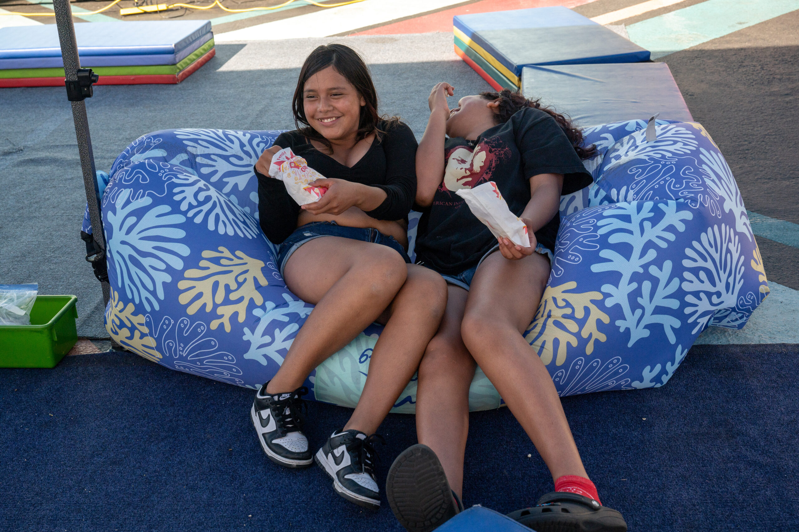 Two dark-haired girls sit on a blue bean bag laughing while eating popcorn.