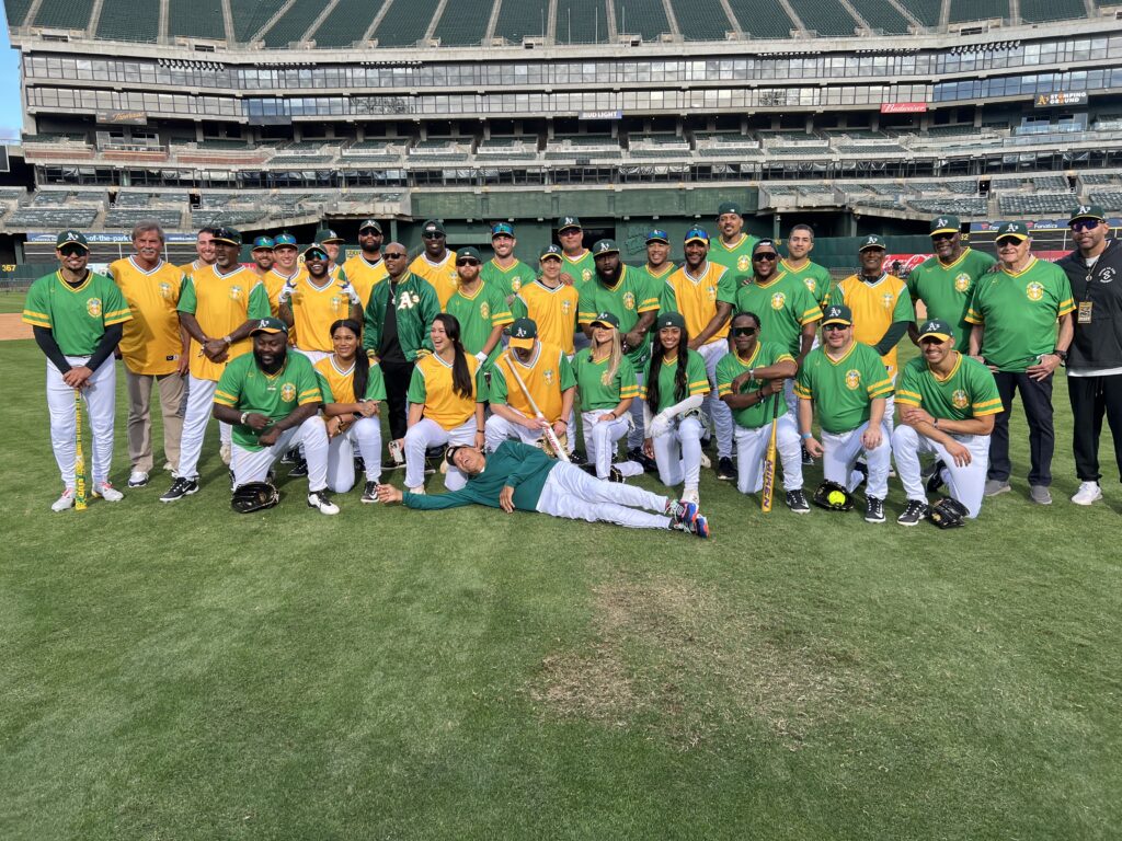 About two dozen players in green and gold shirts pose on the field of the Coliseum