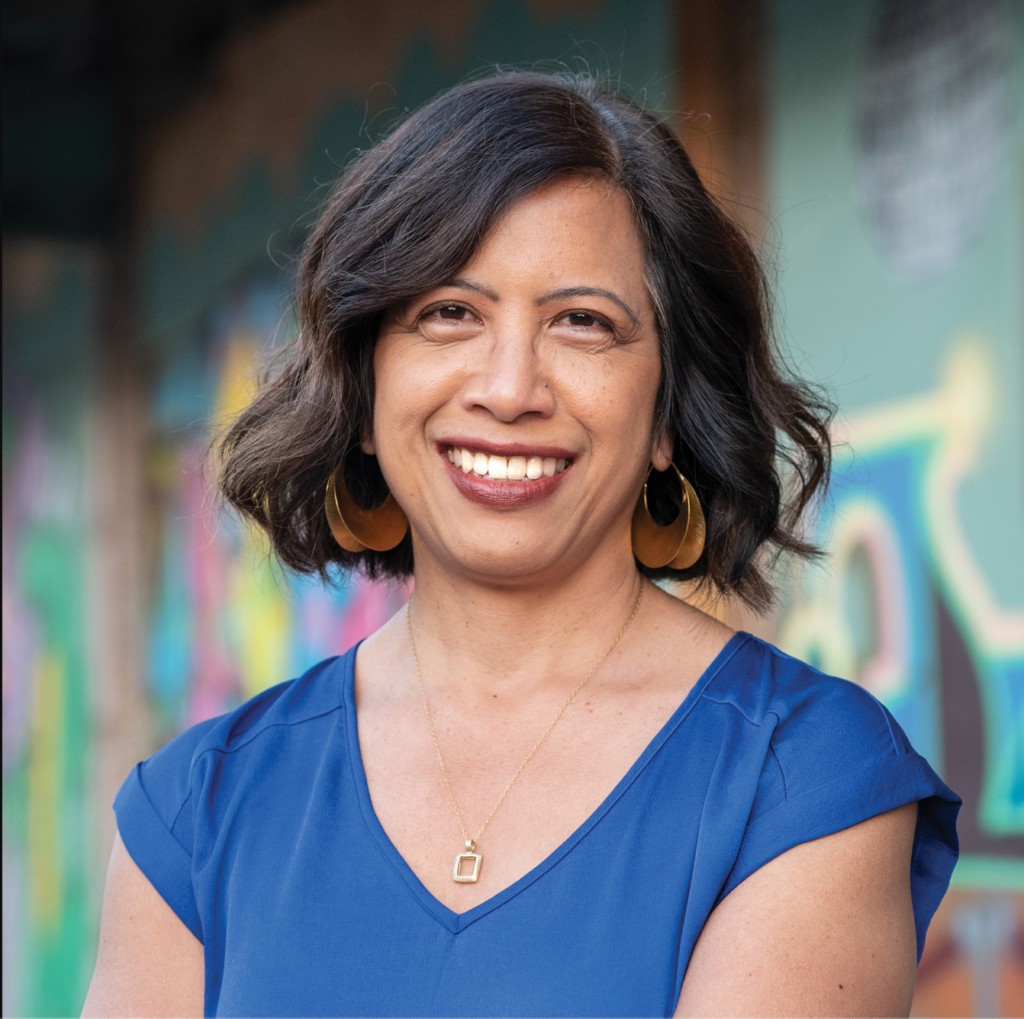 A woman with a blue shirt and hoop earrings smiles for camera