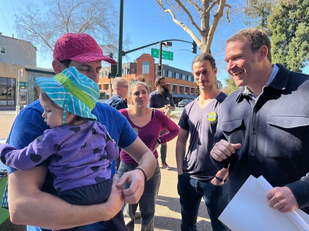 Zac Unger speaking with a supporter holding a toddler.