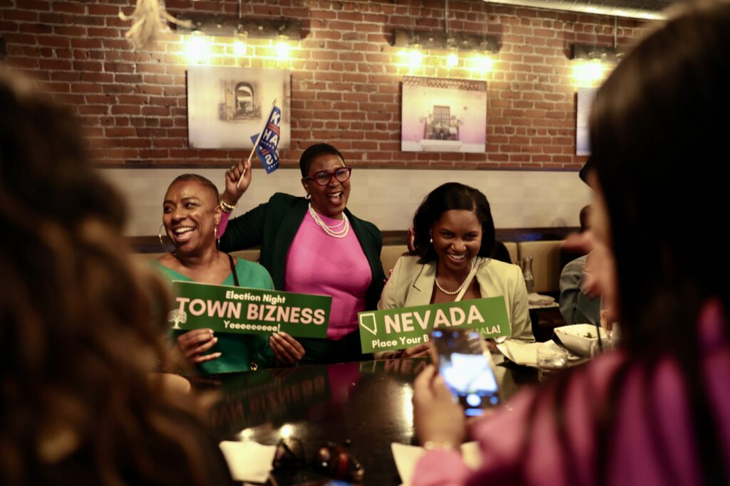 A happy group of women sitting in a restaurant cheering and holding signg.