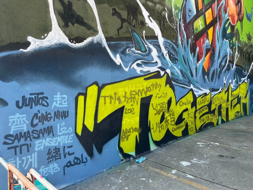 The bottom piece of a colorful mural has the word together in large yellow letters against a blue sea background with a shark's fin poking out.