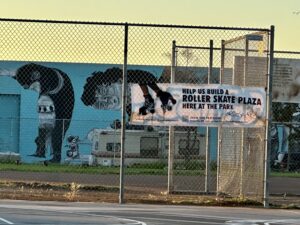 A black and white sign is affixed to a tall chainlink fence behind a basketball court in a park.