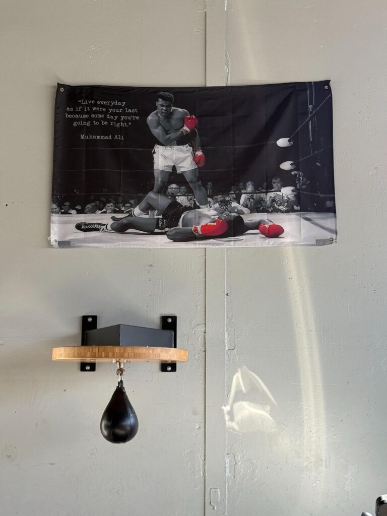 A poster of Muhammad Ali standing over a downed opponent is tacked to a white ball above a punching balloon.