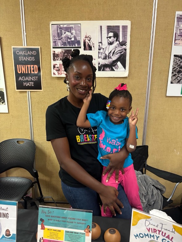 A mom holding her child at a table in a fair.