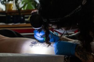 A tatoo artist is applying a flower-shaped tattoo on one's thigh in a dimly-lit room.