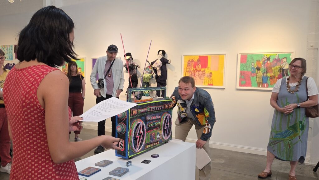 A woman in red dress and a man in colorful shirt is looking at a wood-made colorful radio model