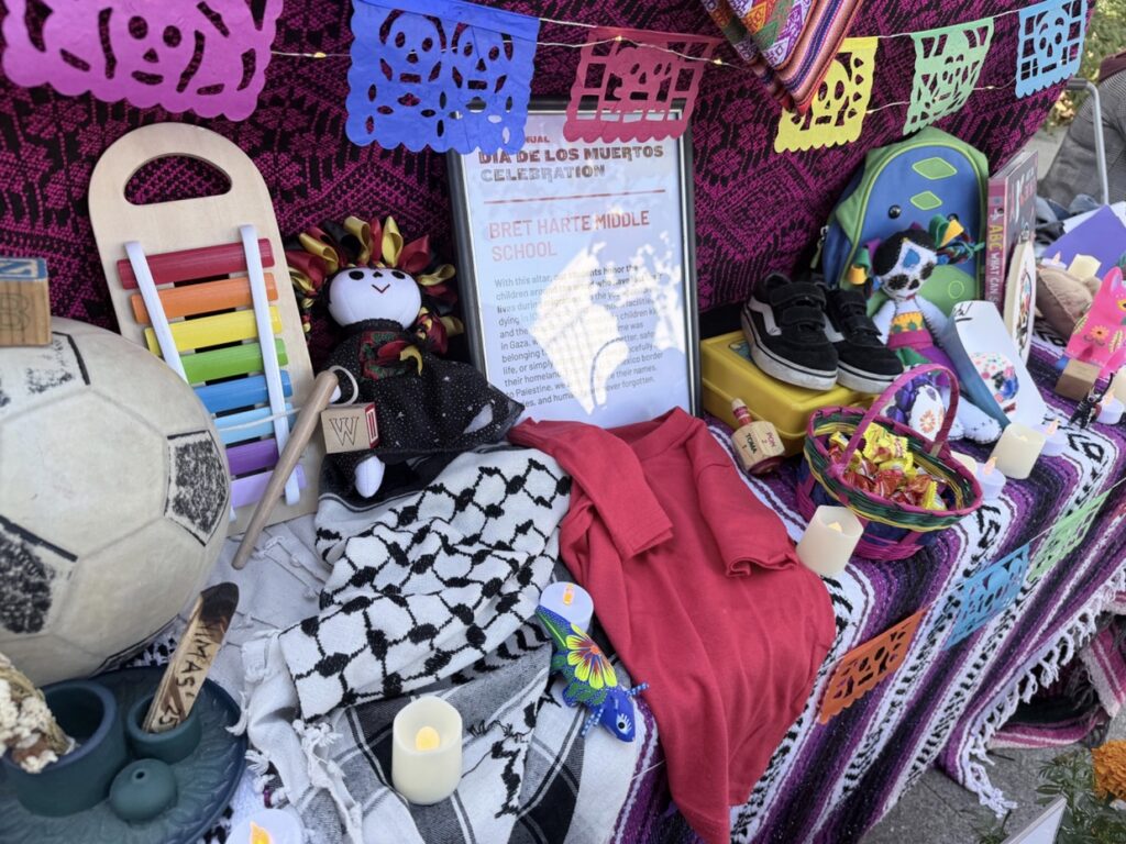 An alter covered with a blanket. On the alter are many personal items, such as a pair of sneaker, a keffiyeh, a big soccer. At the center is a board with a short introduction of the altar."